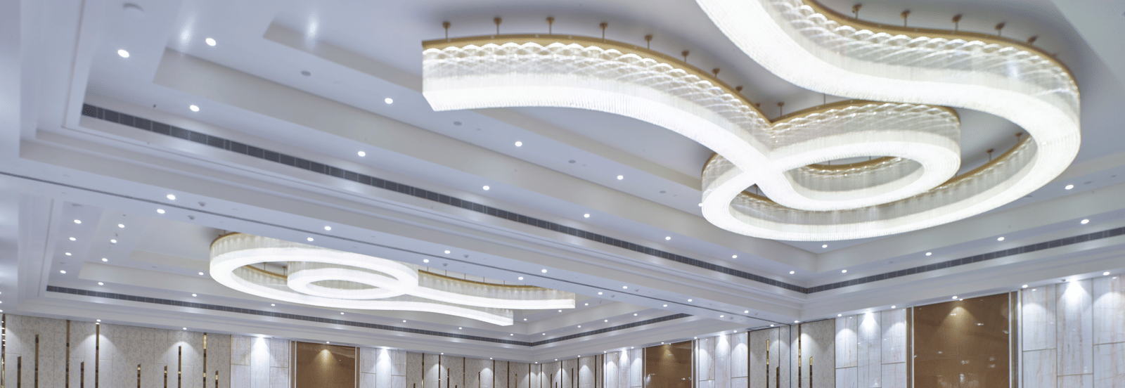 Elegant event space featuring curved ceiling lights and white seating at Merlis Hotel, Coimbatore.