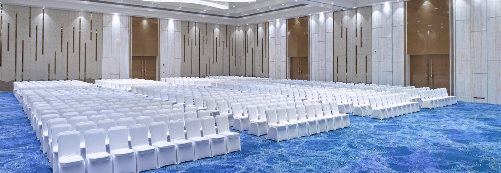 Elegant event space featuring curved ceiling lights and white seating at Merlis Hotel, Coimbatore.