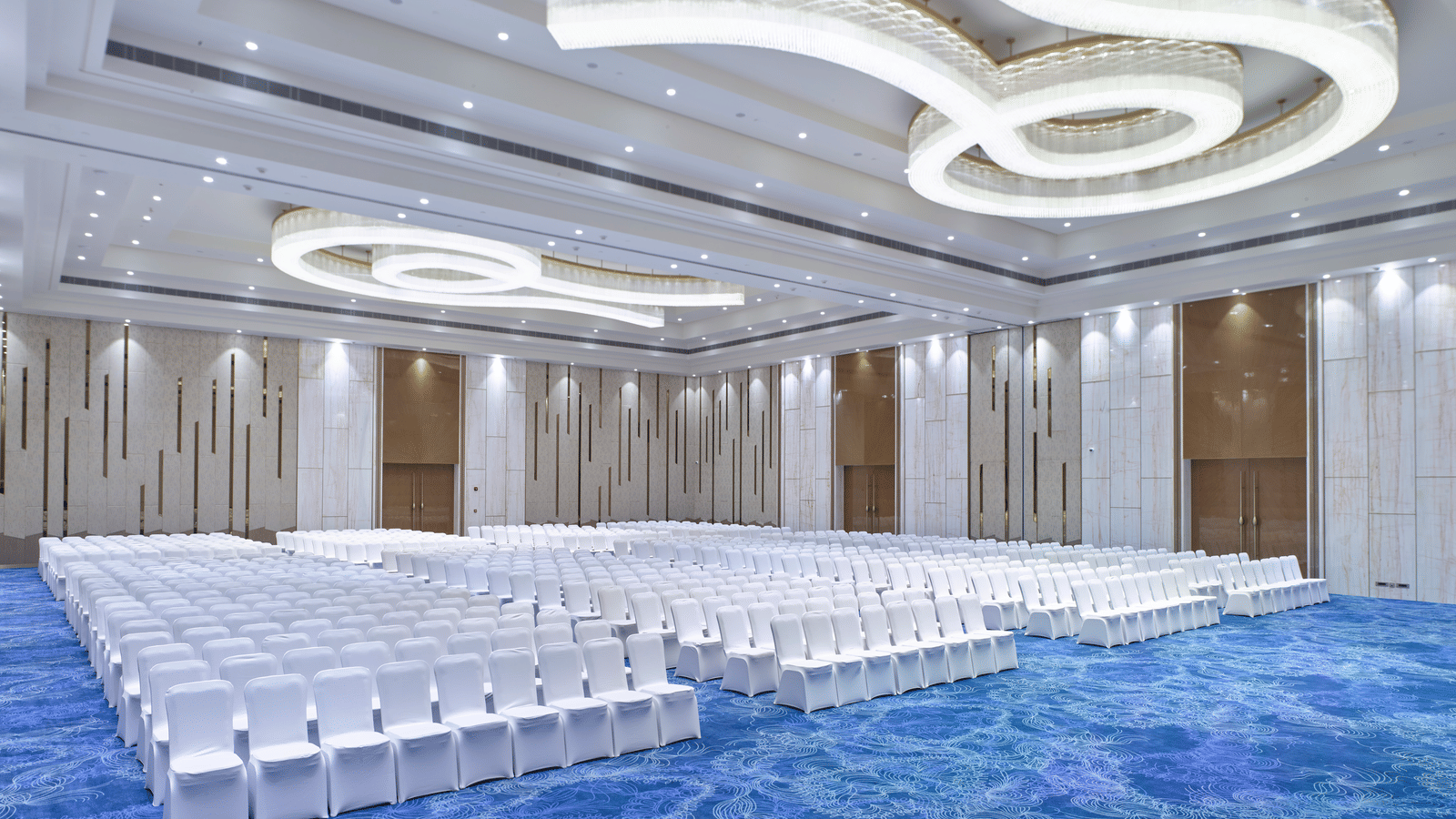 Elegant event space featuring curved ceiling lights and white seating at Merlis Hotel, Coimbatore.