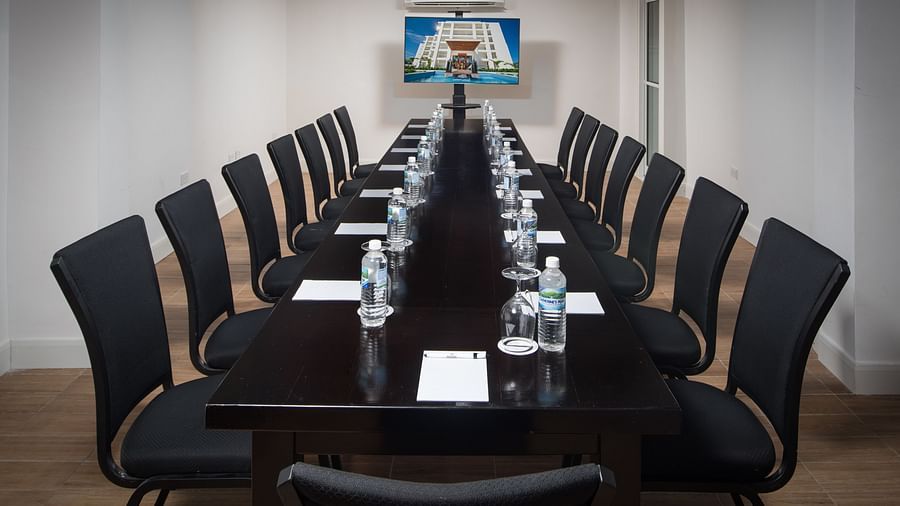 A boardroom with a long table and chairs placed in front of a wall-mounted television - S Hotel Montego Bay, Jamaica