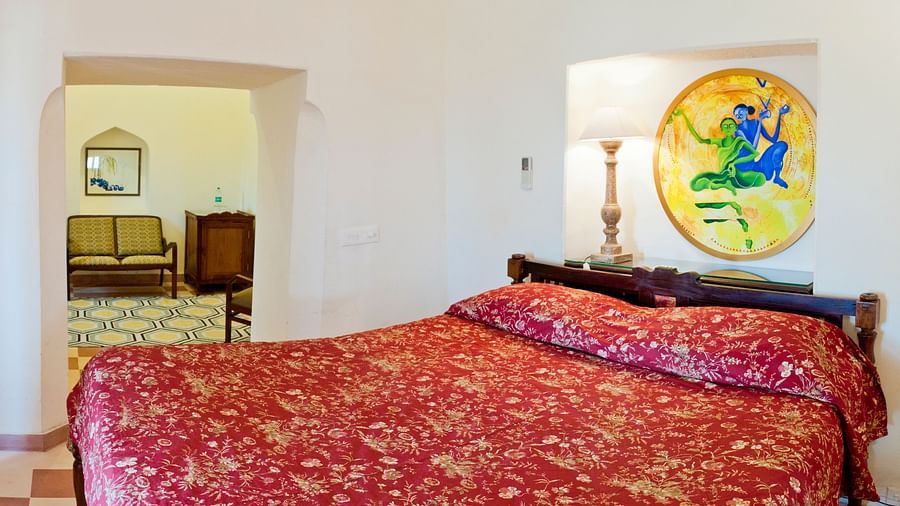 A bedroom with a bed, a lamp, and an arched doorway leading to another room in Tijara Fort-Palace - 19th Century, Alwar.