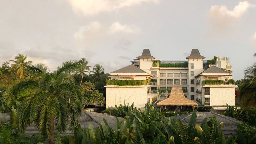 Facade of The Evren, Vagator, featuring the resort amid lush tropical greenary with a cloudy sky in the background.