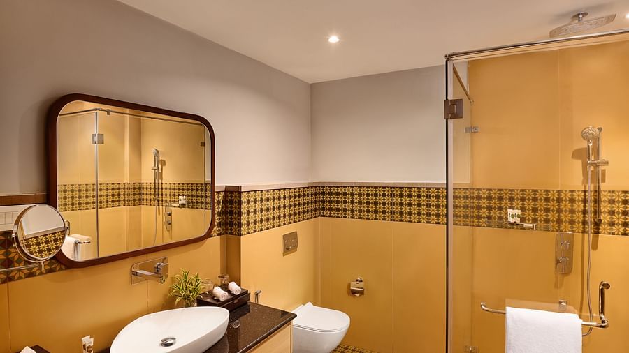 Contemporary bathroom with yellow and black checkered tile accents, vessel sink on a black countertop, large mirror, wall-mounted toilet, and glass-enclosed shower with modern fixtures - Voyage The Solitaire Bliss.