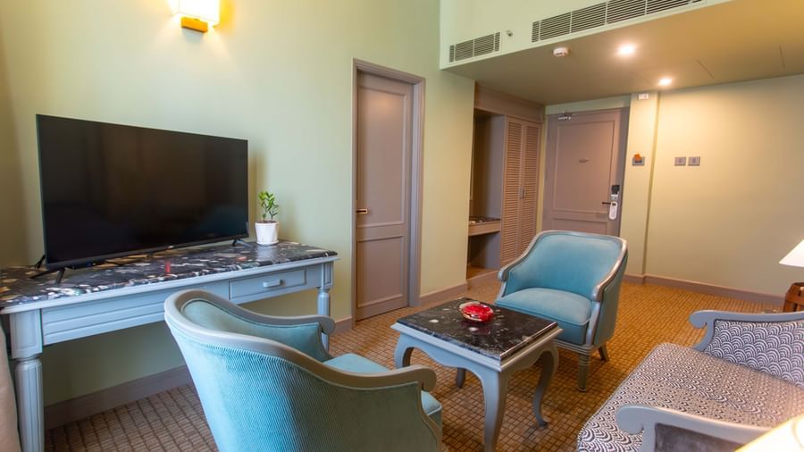  A cosy seating area at Shilton International, Kochi, with comfortable chairs, a coffee table, and a television.