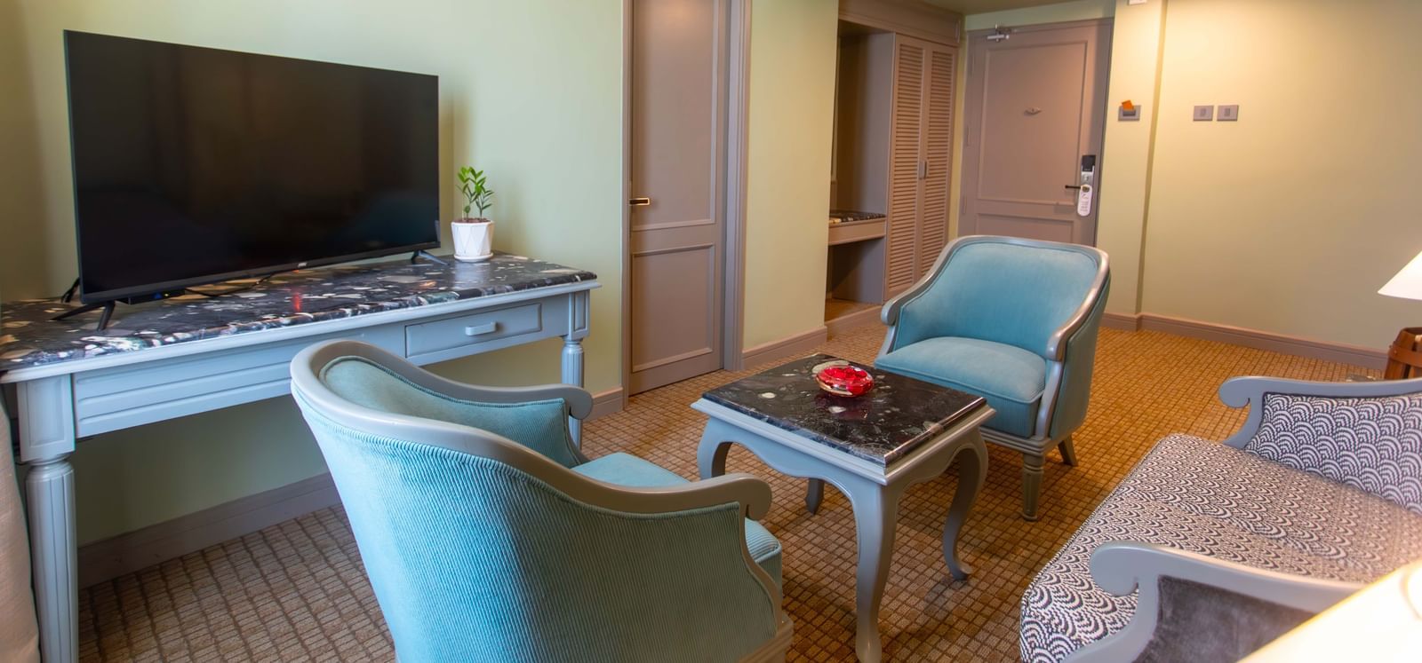  A lounge area in a suite at Shilton International, Kochi, featuring comfortable armchairs, a coffee table, and a television.