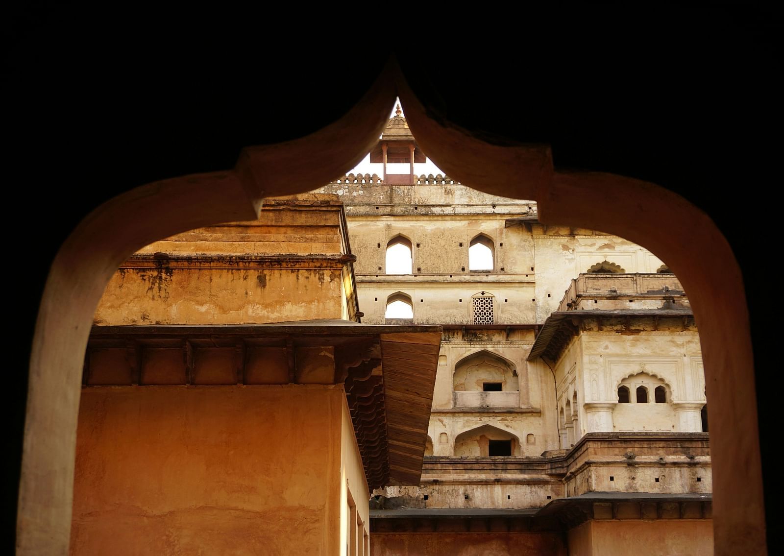 A view from inside a building of an arch and other ancient buildings outdoors.