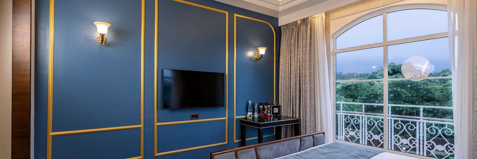 A turquoise coloured wall with golden lines and a wall-mounted television at the Suite at Imperial Goa.