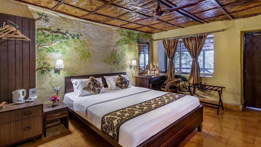A king bed with curtains on the widows and wardrobe on the side inside A.C Deluxe Cottage - Sunderban Tiger Camp, Dayapur
