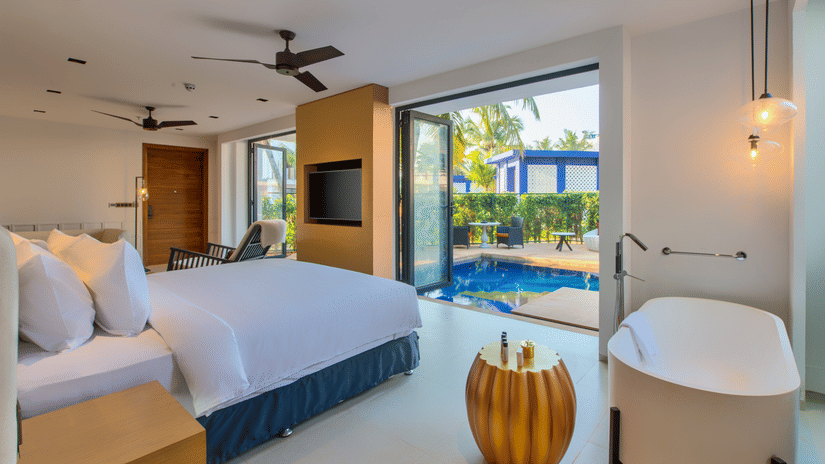 A luxurious hotel room at Azaya Beach Resort Goa featuring a large bed, a freestanding bathtub, and a glass door leading to a private outdoor plunge pool.