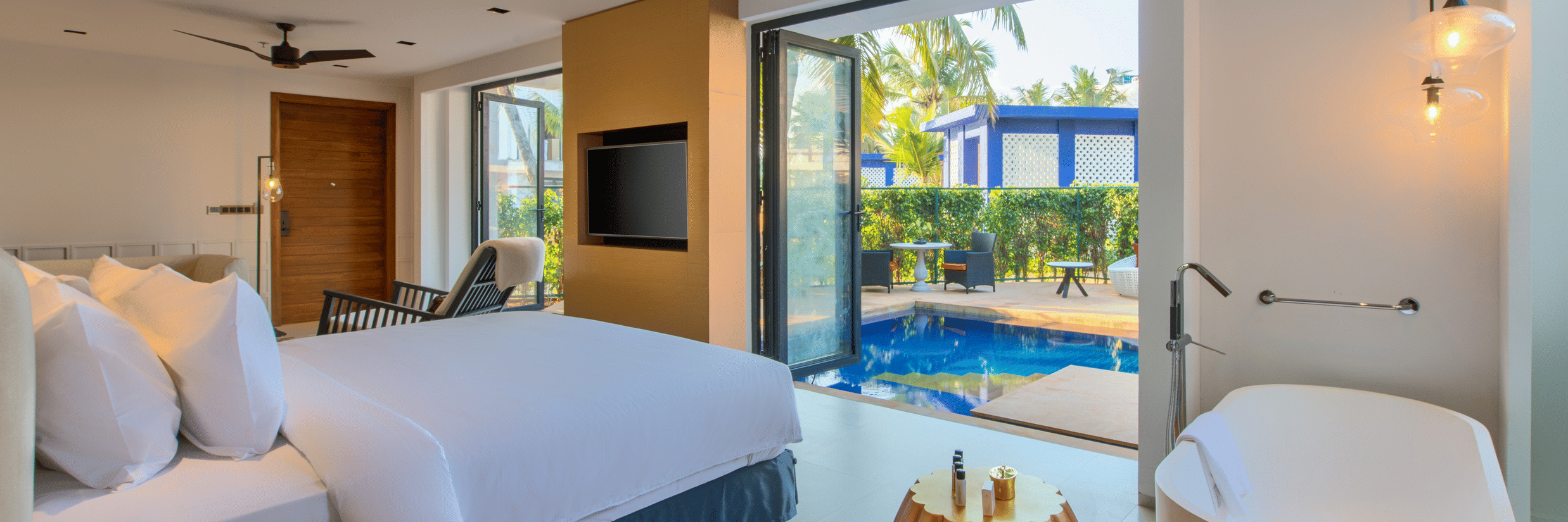A luxurious hotel room at Azaya Beach Resort Goa featuring a large bed, a freestanding bathtub, and a glass door leading to a private outdoor plunge pool.