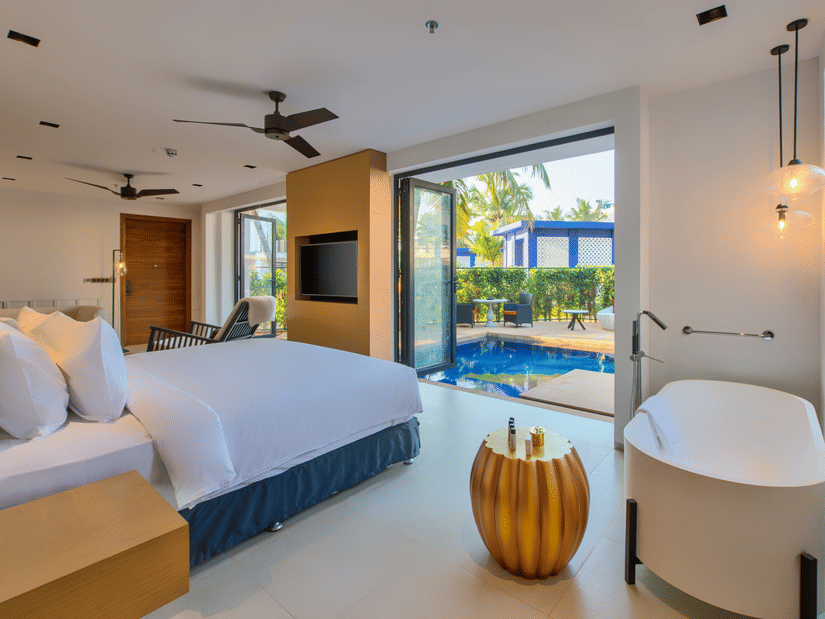 A luxurious hotel room at Azaya Beach Resort Goa featuring a large bed, a freestanding bathtub, and a glass door leading to a private outdoor plunge pool.
