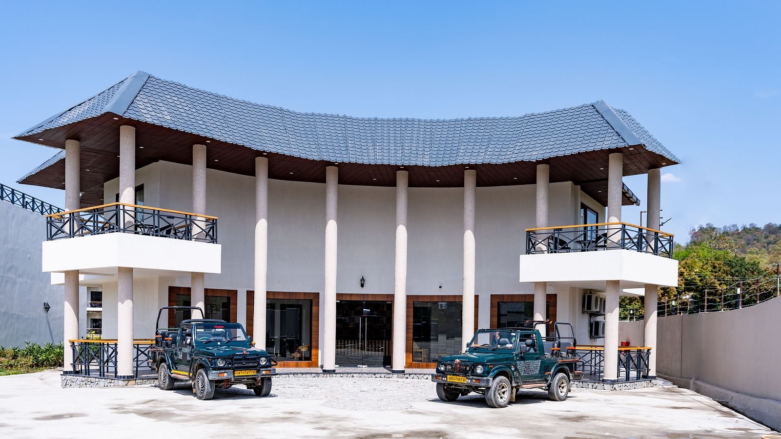 A facade image of the hotel with two jeeps in front seen on a sunny day - Shervani Pebbles & Pines, Corbett