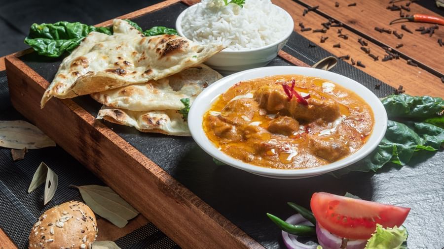 Traditional Indian meal with naan bread, curry, and condiments on wooden board at Best Western Premier Westlands hotel dining venue.