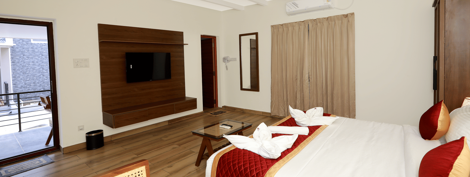 The interiors of the Terrace Cottage featuring a double bed with red-coloured bed runner kept over it, overlooking the entrance door and the TV table at WOW Naturefull Resorts, Yercaud.