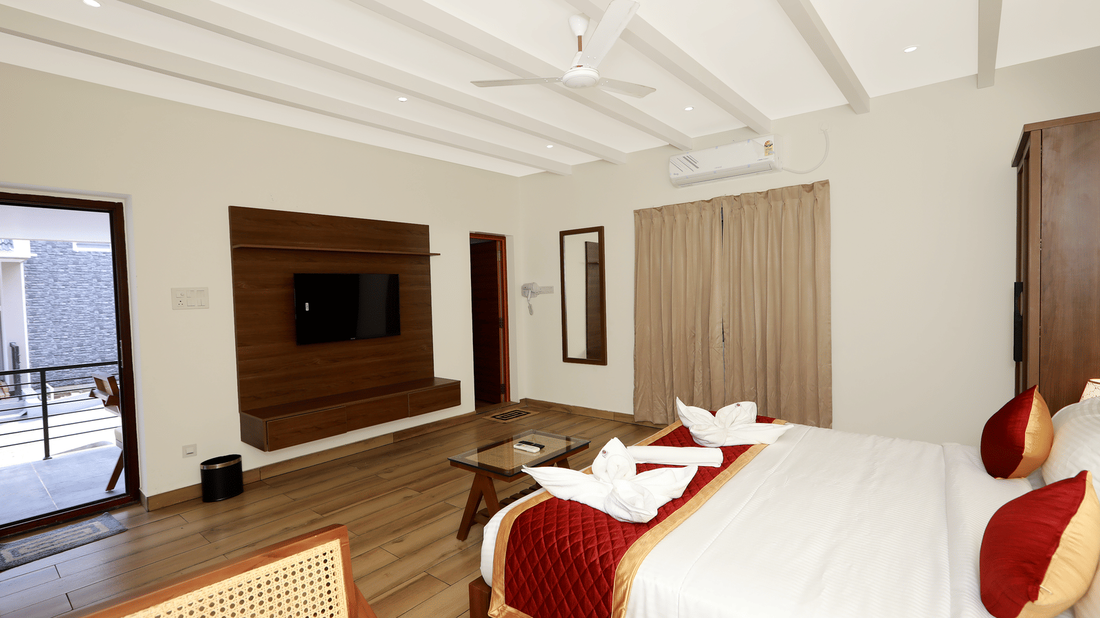 The interiors of the Terrace Cottage featuring a double bed with red-coloured bed runner kept over it, overlooking the entrance door and the TV table at WOW Naturefull Resorts, Yercaud.
