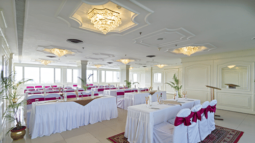 A formal event space with a buffet table at the centre and round tables arranged for seating, decorated in white and red - Clarks Avadh, Lucknow