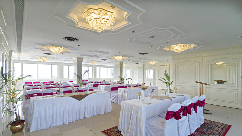 A formal event space with a buffet table at the centre and round tables arranged for seating, decorated in white and red - Clarks Avadh, Lucknow