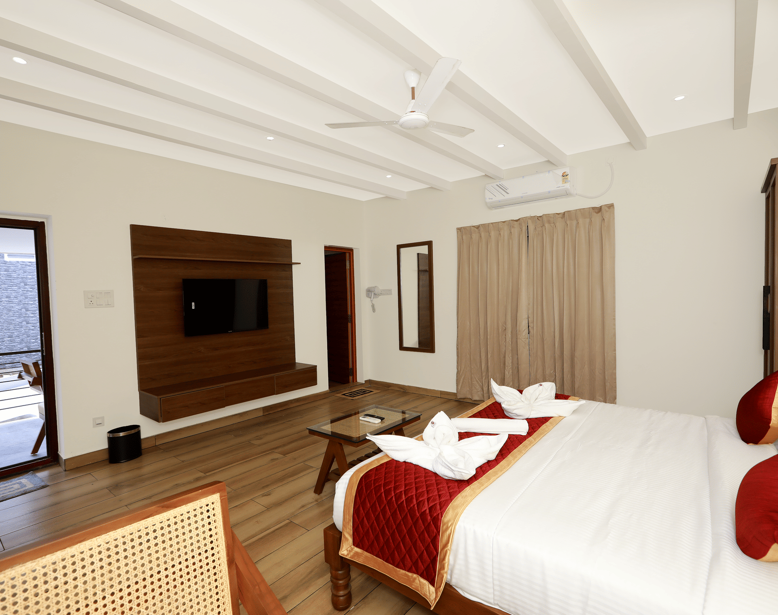 The interiors of the Terrace Cottage featuring a double bed with red-coloured bed runner kept over it, overlooking the entrance door and the TV table at WOW Naturefull Resorts, Yercaud.