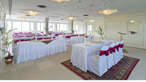 A formal event space with a buffet table at the centre and round tables arranged for seating, decorated in white and red - Clarks Avadh, Lucknow