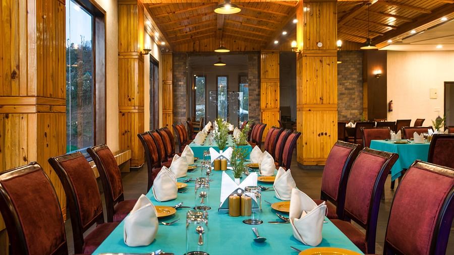  An elegantly set dining table in a spacious restaurant with warm lighting, ready for a delightful culinary experience with a scenic view - Digantaa Resort in Mukteshwar