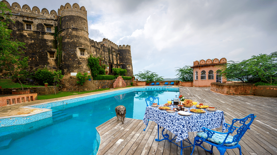 Exterior view of Hill Fort-Kesroli, featuring a table and chair facing a swimming pool under a cloudy sky.