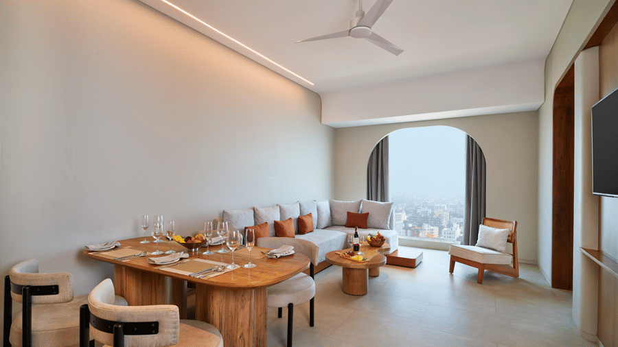 The Oasis Suite bedroom at Swosti Premium Beach Resorts, Puri, with living area featuring a dining table with chairs, a sofa, and large windows.