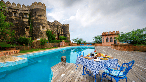  Exterior view of Hill Fort-Kesroli, featuring a table and chair facing a swimming pool under a cloudy sky.