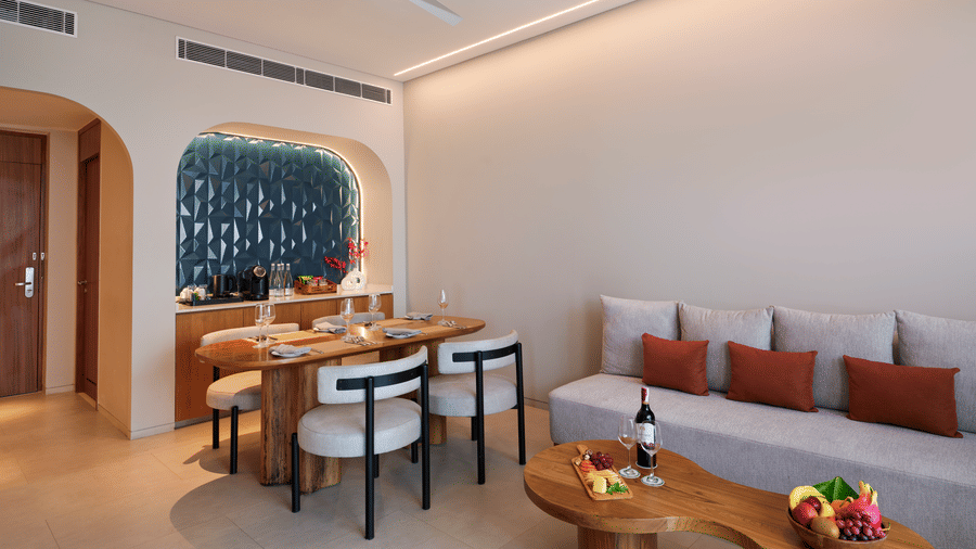 The Oasis Suite bedroom at Swosti Premium Beach Resorts, Puri, with living area featuring a dining table with chairs, a sofa, and tables.