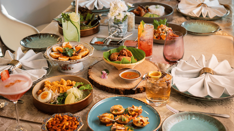 A table set with a variety of colourful dishes, drinks, and garnishes, featuring appetizers, main courses, and beverages.
