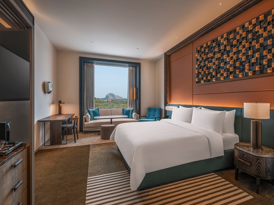 View of the Premium King room at The Residency Signature Madurai with a king bed, large window, green table lamp, and warm ambient lighting.