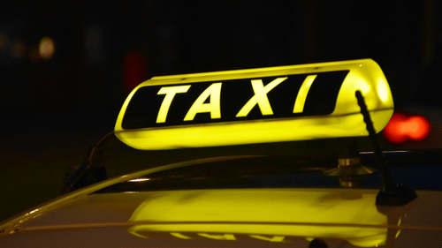 Taxi with an illuminated sign parked for passenger transport at night.