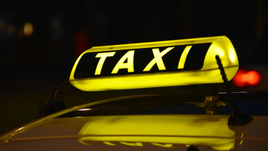 Taxi with an illuminated sign parked for passenger transport at night.