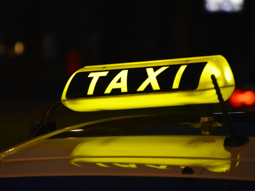 A close up of the Taxi signage on top of a yellow taxi, with the lights on, indicating it is available for hire.