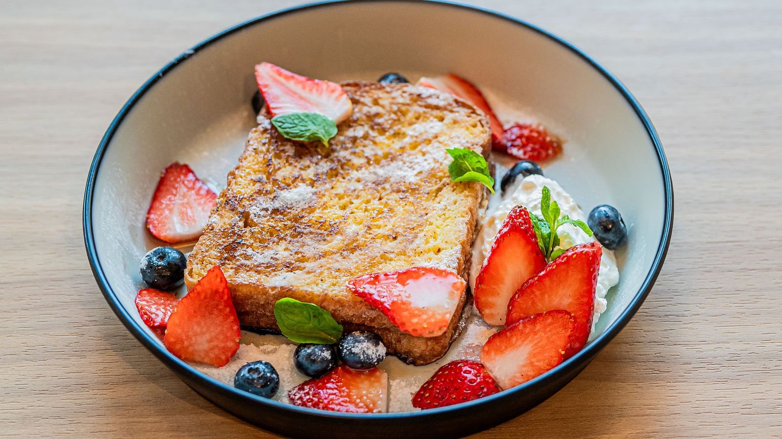 A deep plate with bread toast topped with slices of strawberries and blueberries at Indie Stays Mumbai International Airport.