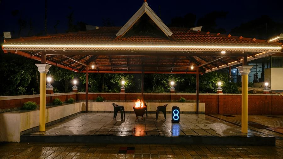 A beautiful night shot of the illuminated pavilion at Bhuthanakadu Retreat, showing the warm glow of lights reflecting off the wet floor after a rainfall.