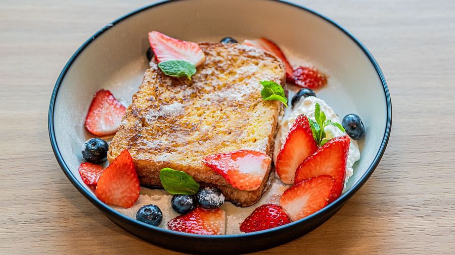 A deep plate with bread toast topped with slices of strawberries and blueberries at Indie Stays Mumbai International Airport.