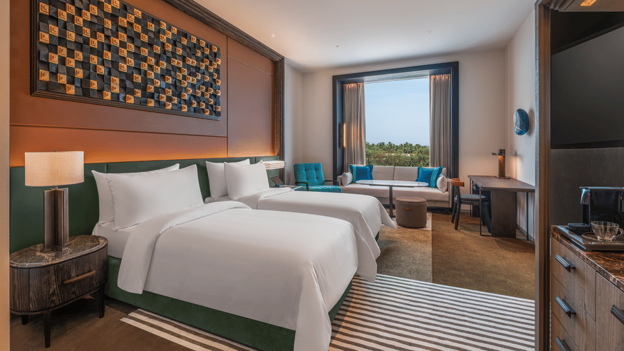 Hotel room at The Residency Signature Madurai equipped with two neatly made twin beds, a side desk, a window lounge, and wood panelling on the wall.