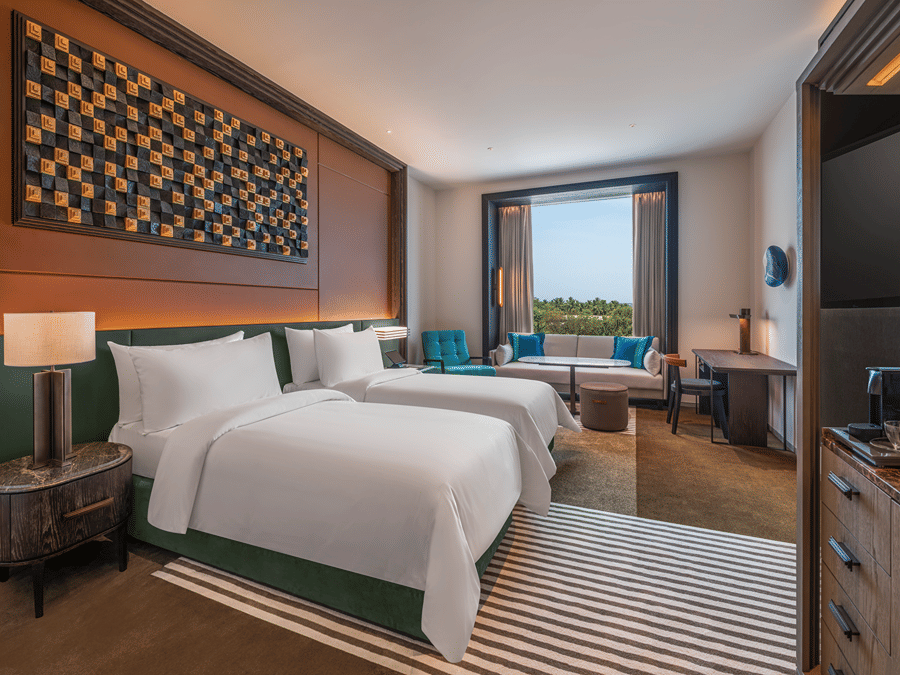 View of the Premium Twin room at The Residency Signature Madurai with twin beds, wooden panelling, work desk, green table lamp, and warm ambient lighting.