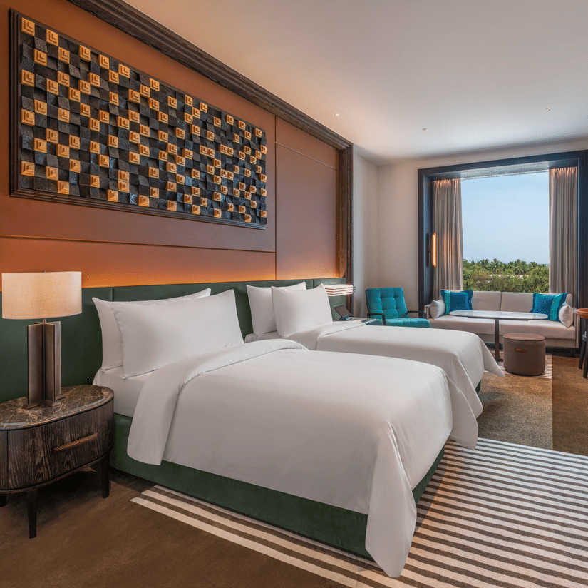 View of the Premium Twin room at The Residency Signature Madurai with twin beds, wooden panelling, work desk, green table lamp, and warm ambient lighting.