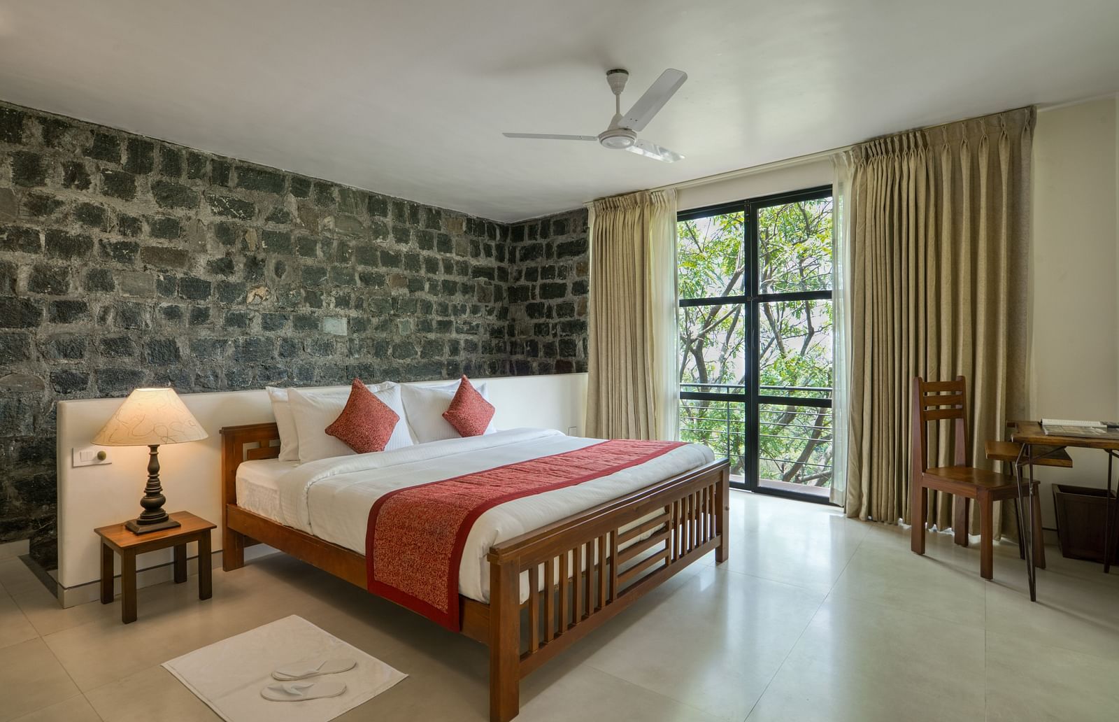 A luxurious bedroom with a stone feature wall, large windows, a comfortable bed, and a scenic view of the greenery outside.  | Mango Hill, Yercaud