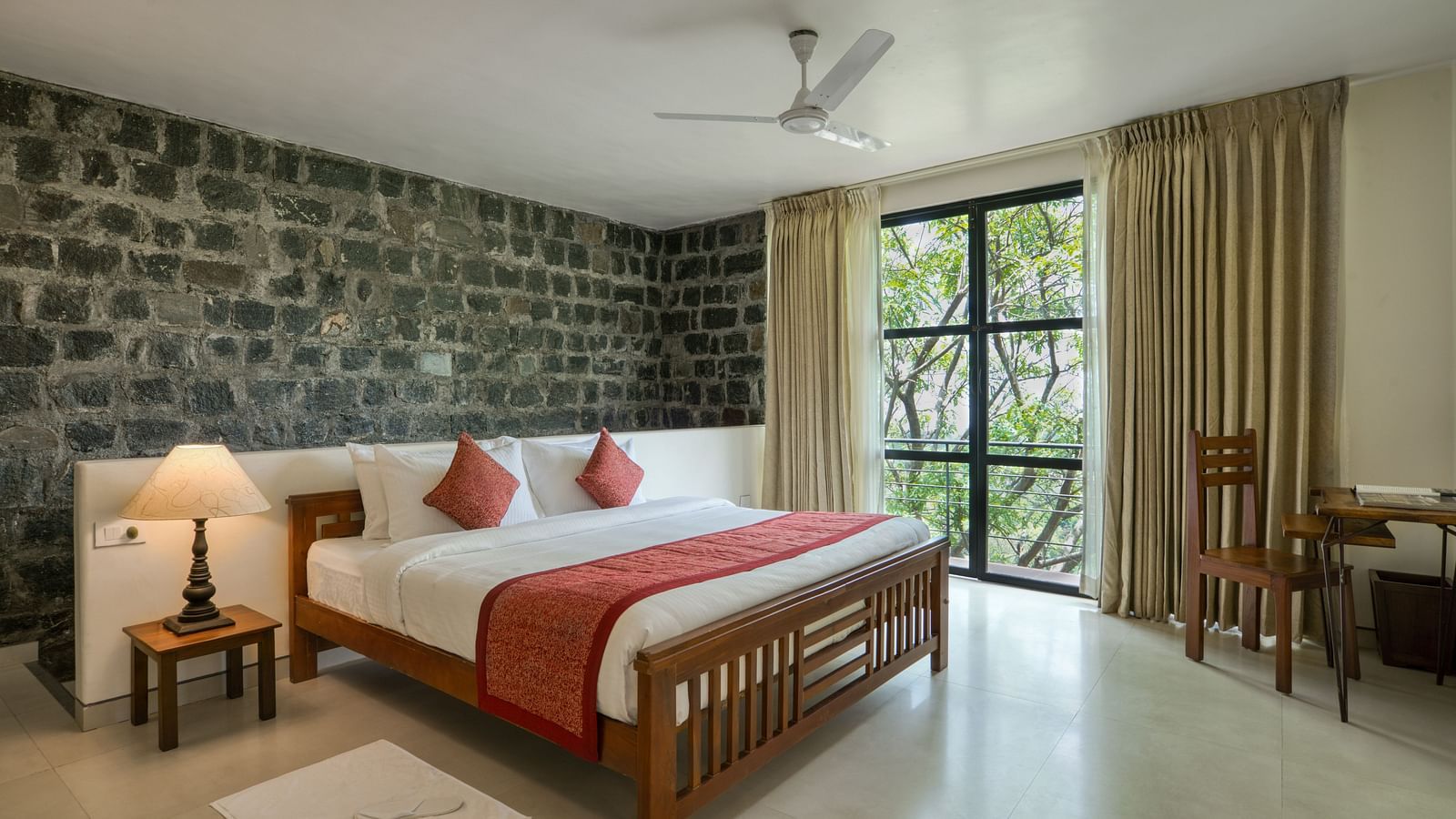 A luxurious bedroom with a stone feature wall, large windows, a comfortable bed, and a scenic view of the greenery outside.  | Mango Hill, Yercaud