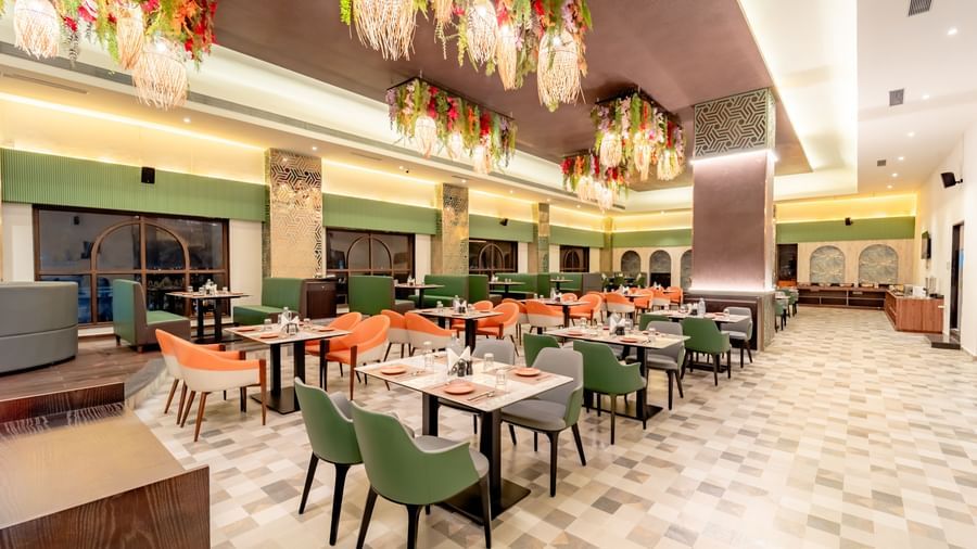 Dining area with green and orange chairs and decorative hanging elements | Pravasa Hotel, Vijayapura