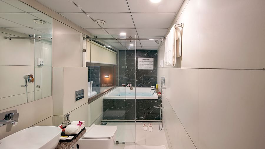 A bright hotel bathroom showcases a contemporary white sink, toilet, and a bathtub enclosed by glass, with towels neatly arranged -  SK Lords Inn Ahmedabad