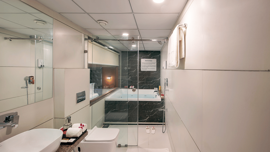 A bright hotel bathroom showcases a contemporary white sink, toilet, and a bathtub enclosed by glass, with towels neatly arranged -  SK Lords Inn Ahmedabad