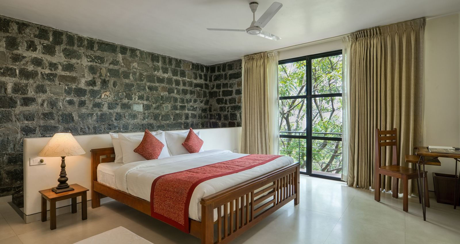 A luxurious bedroom with a stone feature wall, large windows, a comfortable bed, and a scenic view of the greenery outside.  | Mango Hill, Yercaud