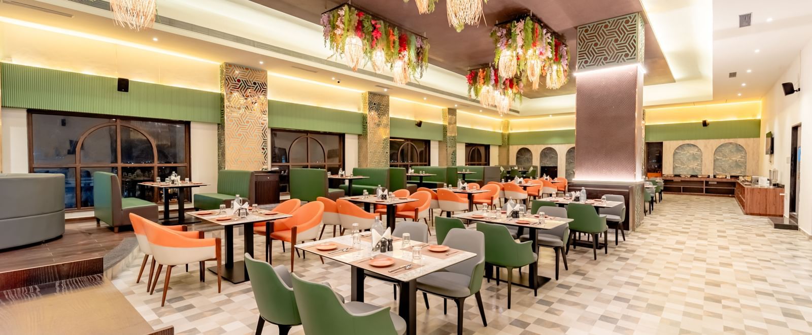 Dining area with green and orange chairs and decorative hanging elements | Pravasa Hotel, Vijayapura