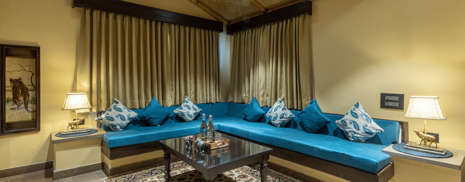A living area at Aamaghati Wildlife Resort with plush blue sofas, tasteful décor, and soft lighting perfect for unwinding with family or friends.