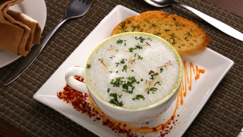 Creamy soup served in a white bowl, garnished with herbs, accompanied by toasted garlic bread on a square plate with spice decor at Southern Express, Uday Suites