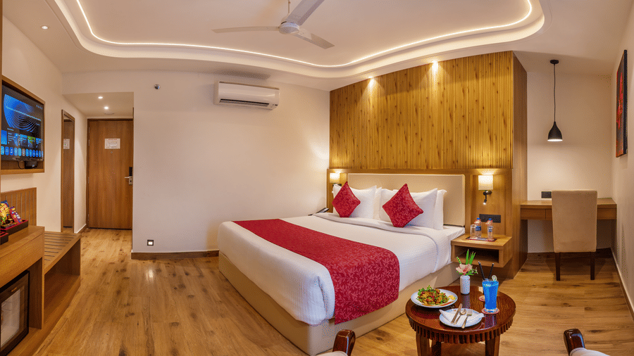 A hotel bedroom interior at Lords Inn Katra showing a king size bed, a wall mounted television, and a wooden door leading to the entrance corridor.