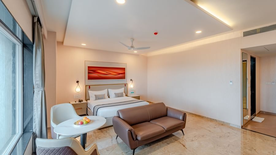  A spacious room with a king-size bed, a sofa, and a wall-mounted television | Studio Suite | Pravasa Hotel, Vijayapura